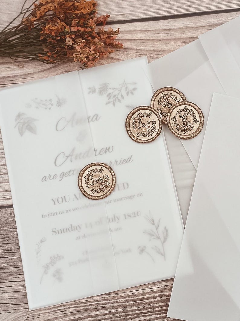 May include: A white wedding invitation with a gold wax seal featuring the initials "J&M". The invitation is decorated with delicate floral illustrations and the text "Clara and Andrew are getting married on Sunday 14 of July 1820".