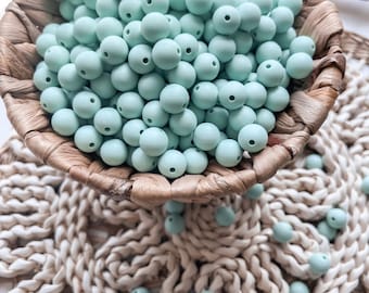 May include: A wicker basket filled with light blue silicone beads. The beads are scattered on a beige crocheted surface.