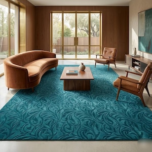 Puede incluir: Una alfombra rectangular grande de color verde azulado profundo con un patrón botánico de remolinos en relieve tono sobre tono. La alfombra está colocada en una habitación con un sofá naranja curvo, dos sillones de madera y una mesa de centro.