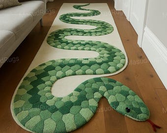Puede incluir: Una alfombra larga verde con forma de serpiente con diferentes tonos de verde, creando un patrón texturizado en forma de escamas. La alfombra tiene un fondo crema y una lengua roja. La cabeza de la serpiente está en la parte inferior, con ojos negros.