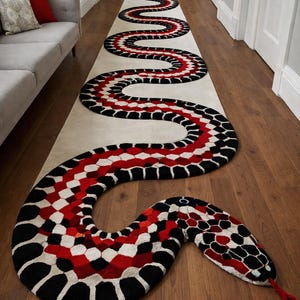 Peut inclure: Un long tapis décoratif en forme de serpent dans un couloir. Le tapis présente un motif de formes géométriques noires, rouges et blanches. La tête du serpent est au bout du tapis, avec une langue rouge. Le tapis est sur un parquet.