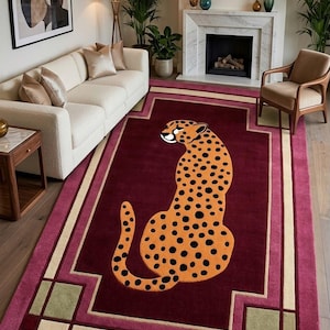 May include: A rectangular area rug featuring a central orange cheetah with black spots on a deep burgundy background. The rug has a geometric border in shades of cream, dark red, and muted green, creating a structured frame around the animal motif.