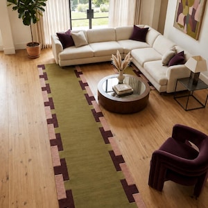 May include: A long rectangular area rug featuring a solid olive green center panel bordered by a geometric pattern of alternating dark brown and dusty pink rectangular blocks along the two long edges, creating a structured and repeating border design.