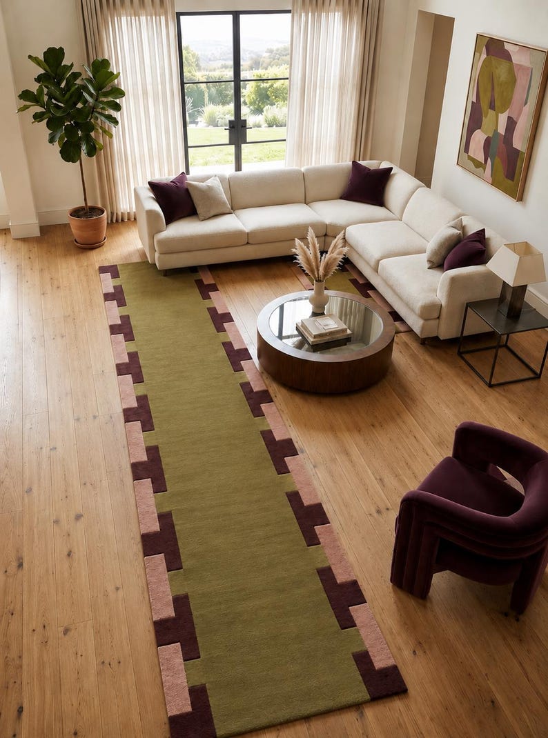 May include: A long rectangular area rug featuring a solid olive green center panel bordered by a geometric pattern of alternating dark brown and dusty pink rectangular blocks along the two long edges, creating a structured and repeating border design.