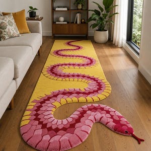 Peut inclure: Un tapis jaune avec un motif de serpent en rose et rouge. Le corps du serpent serpente sur le tapis, avec une tête et une langue détaillées. Le tapis est posé sur un parquet, avec un canapé et des plantes en arrière-plan.