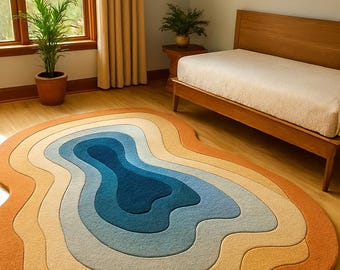 Könnte beinhalten: Ein farbenfroher Teppich mit organischen Formen und einem mehrschichtigen Design. Die Farbpalette reicht von tiefem Blau in der Mitte bis zu helleren Blau-, Gelb- und Orangetönen. Der Teppich liegt auf einem Holzboden in einem Raum mit einem Bett.