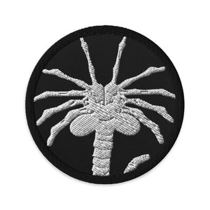 May include: A white embroidered alien creature with eight legs on a black circular patch.