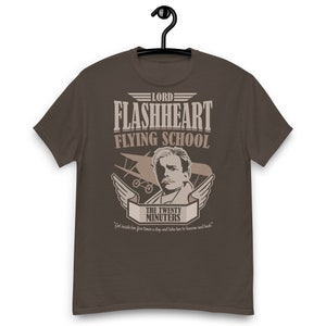 May include: A brown t-shirt with a vintage-style graphic design featuring a cartoon pilot, an airplane, and the text "Lord Flashheart Flying School The Twenty Minuters" with the tagline "Get inside her five times a day and take her to heaven and back."