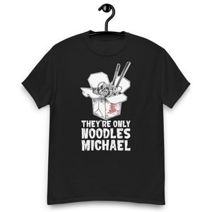 Op de afbeelding: Zwart T-shirt met een witte afbeelding van een Chinese afhaalkarton met eetstokjes en noedels. De tekst "They're only noodles Michael" staat onder de doos.