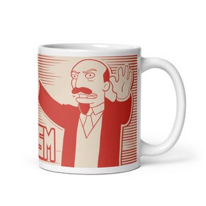 May include: White ceramic mug with a red and white illustration of a cartoon character with a mustache, wearing a red suit and raising his hand. The text "EM" is visible at the bottom of the mug.