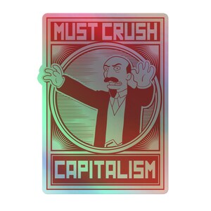 May include: Holographic sticker with the text "MUST CRUSH CAPITALISM" in red block letters. The sticker features a cartoon illustration of a man in a suit with his arms outstretched. The background has a gradient of red, green, and blue.