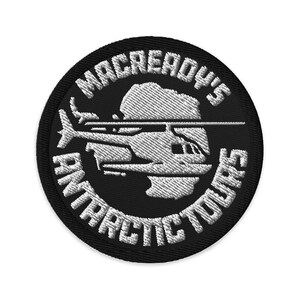 May include: Embroidered patch with the text "MACREADY'S ANTARCTIC TOURS" in white on a black circular background. A white helicopter graphic is centered within the design.