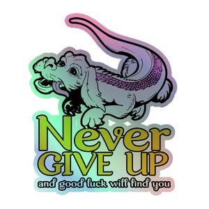 Op de afbeelding: Een holografische sticker met een gestileerd draakachtig wezen met een lange staart en schubben, geplaatst boven de tekst "Never GIVE UP and good luck will find you" in een vet, meerkleurig verlooplettertype op een reflecterend oppervlak.