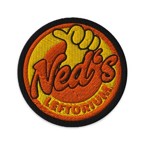 Pode incluir: Uma caneca de cerâmica branca com uma alça preta e o texto "But First, Coffee" em negrito preto. A caneca está sobre um fundo desfocado, sugerindo um ambiente acolhedor.