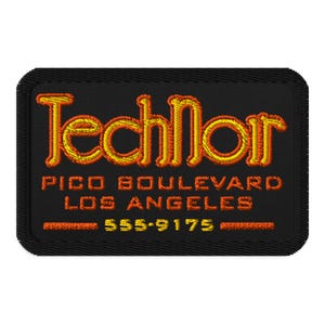 May include: Black rectangular patch with embroidered text in orange and yellow. The text reads "TechNoir" above "PICO BOULEVARD LOS ANGELES" and a phone number. The patch has a stitched border.