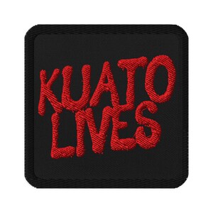 Könnte beinhalten: Quadratischer schwarzer Aufnäher mit den gestickten Worten "KUATO LIVES" in roter, stilisierter Schrift. Der Aufnäher hat einen schwarzen Rand und ein strukturiertes Aussehen, was darauf hindeutet, dass er aus Stoff besteht.