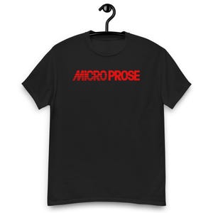 May include: A black short-sleeved t-shirt featuring the text MICRO PROSE printed in red across the chest. The word MICRO is stylised with horizontal lines through the letters, while the word PROSE is in a solid red font. The shirt is displayed on a hanger.