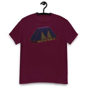 May include: A maroon short-sleeved t-shirt featuring a graphic of a three-dimensional trapezoidal shape with a blue and yellow grid pattern. The word MASTERTRONIC is printed in yellow capital letters on the front base of the graphic design.