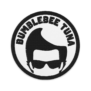 Puede incluir: Parche bordado circular con el texto "BUMBLEBEE TUNA". El diseño presenta una silueta negra de una persona con gafas de sol y un peinado tupé, sobre un fondo blanco, dentro de un borde negro.