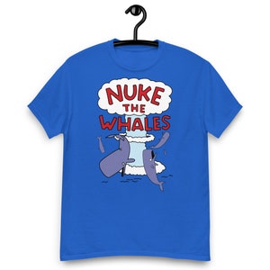 May include: A bright blue short-sleeve t-shirt featuring a graphic print of a mushroom cloud with the red text NUKE THE WHALES above several cartoon whales swimming in the ocean. The design is centered on the chest of the crew neck shirt.