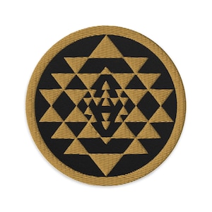 Op de afbeelding: Geborduurde patch met een Sri Yantra-ontwerp. De patch heeft een zwart midden met een geometrisch patroon van gouden driehoeken. De buitenrand is goudkleurig en creëert een cirkelvorm.