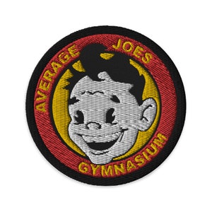May include: An embroidered patch in black, red and yellow featuring a cartoon character's face. The text around the character reads "Average Joes Gymnasium".