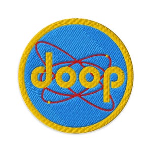 Könnte beinhalten: Runder, gestickter Aufnäher mit dem Wort "doop" in Gelb auf blauem Hintergrund mit einem roten atomähnlichen Design. Der Aufnäher hat einen gelben Rand.
