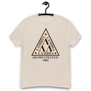 May include: A light beige short-sleeve t-shirt featuring a black triangular graphic on the chest. The triangle contains the word LAMBDA repeated along its sides, with three Greek lambda symbols in the center. Below, the text reads ADAMS COLLEGE 1984.