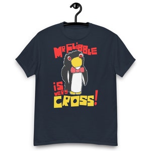 May include: Navy blue t-shirt featuring a cartoon penguin with a red bow tie and the text "Mr. Fribble is Very Cross!" in red and yellow. The penguin has a yellow beak and is set against a white background.