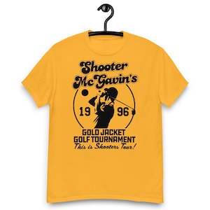 Puede incluir: Camiseta amarilla mostaza con un gráfico negro que presenta el texto "Shooter McGavin's" sobre una silueta de golfista. El diseño incluye los años "19" y "96" y el texto "GOLD JACKET GOLF TOURNAMENT This is Shooters Tour!"