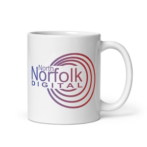 以下が含まれることがあります： 白いセラミック製のマグカップで、赤と紫のロゴが書かれており、「North Norfolk Digital」と円形のデザインが描かれています。