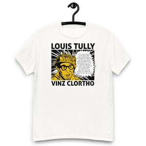 Op de afbeelding: Wit T-shirt met een pop-art-achtige afbeelding van een man met een helm en bril. De afbeelding bevat de tekst "LOUIS TULLY" en "VINZ CLORTHO" en een tekstballon met tekst. Het ontwerp is in zwart en geel.
