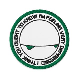 Peut inclure: Écusson rond brodé avec un centre blanc et une bordure verte. Le texte "I THINK YOU OUGHT TO KNOW I'M FEELING VERY DEPRESSED" est brodé en noir sur le bord. Une ligne noire et deux triangles verts sont au centre.