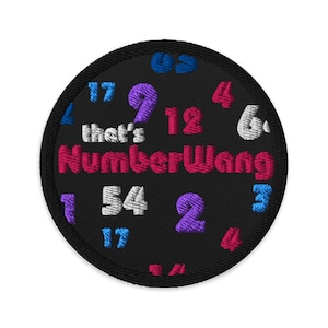 Może przedstawiać: Okrągła, haftowana naszywka na czarnym tle. Naszywka zawiera napis "that's NumberWang" w kolorze różowym, otoczony różnymi liczbami w kolorze niebieskim, fioletowym i białym. Naszywka ma czarną obwódkę.