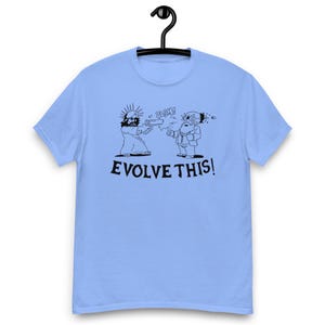 Può includere: T-shirt azzurra con grafica umoristica. Il disegno presenta una rappresentazione a cartoni animati di una figura con un'aureola che spara a un'altra figura. Il testo "EVOLVE THIS!" è stampato sotto le figure.