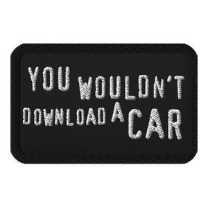 May include: Black rectangular patch with white embroidered text: "YOU WOULDN'T DOWNLOAD A CAR". The patch has a stitched border and a textured appearance.