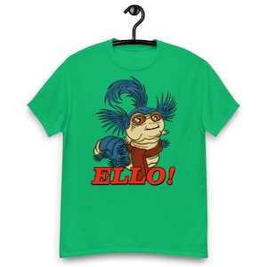 May include: Green t-shirt featuring a cartoon illustration of a blue and brown creature with a red scarf. The creature is saying "ELLO!"