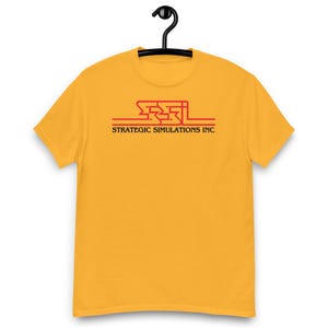 Könnte beinhalten: Ein senfgelbes Kurzarm-T-Shirt mit einem roten Grafiklogo auf der Brust. Das Logo zeigt die stilisierten Buchstaben SSI über dem Text STRATEGIC SIMULATIONS INC in einer schwarzen Serifenschrift, zentriert auf der Vorderseite des Kleidungsstücks.