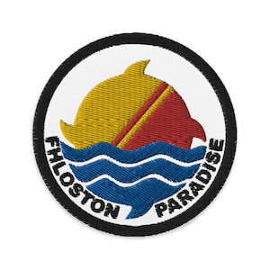 May include: Embroidered patch featuring a yellow dolphin leaping over blue waves, with a red and yellow sail. The patch is circular, with the words "FHLOSTON PARADISE" in white text around the edge, set against a black border.