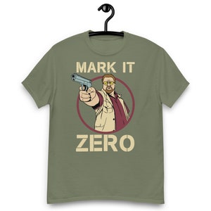 Może przedstawiać: Zielona koszulka z kreskówkowym obrazkiem mężczyzny trzymającego pistolet i tekstem "MARK IT ZERO" w stylu vintage.