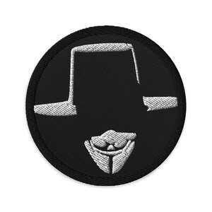 Puede incluir: Parche redondo bordado en negro con un diseño blanco estilizado. El diseño incluye un sombrero, una línea horizontal y una máscara estilizada. El parche tiene un borde negro.