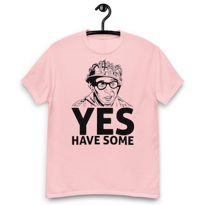 Op de afbeelding: Lichtroze t-shirt met een zwart-witte afbeelding van een man met een bril en een kroon. De tekst "YES HAVE SOME" staat eronder.