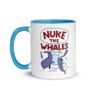 May include: White ceramic mug with a blue handle and interior. The mug features a cartoon graphic of a mushroom cloud with the text "NUKE THE WHALES" in red and white. Two purple whales are depicted.