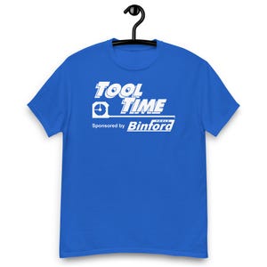 Op de afbeelding: Koningsblauw T-shirt met de witte tekst "TOOL TIME", met een afbeelding van een meetlint. Daaronder staat "Sponsored by Binford TOOLS". Het shirt hangt aan een zwarte hanger.