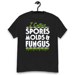 Op de afbeelding: Zwart T-shirt met de tekst "I Collect Spores, Molds & Fungus" in wit, groen en geel. Het ontwerp bevat een druipende groen-gele rand en een zwarte hanger.