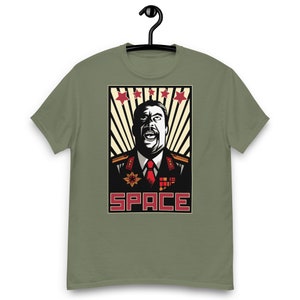 May include: A green t-shirt featuring a vintage-style poster design of a man in military uniform with a red star on his hat. The poster reads "SPACE" in red letters.