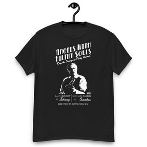 Może przedstawiać: Czarny T-shirt z białym nadrukiem przedstawiającym mężczyznę w białej koszuli z tekstem "Angels with Filthy Souls" i "Keep the Change ya Filthy Animal". Grafika zawiera również tekst "VHS", "Ralph Foody as Johnny", "Michael Guido as Snakes", i "Directed by John Hughes".