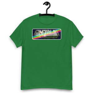May include: A bright green short-sleeve t-shirt featuring a rectangular graphic on the chest. The graphic displays the word GREMLIN in a metallic, outlined font set against a dark background with a vibrant, multi-coloured rainbow light streak.