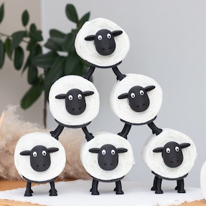 Op de afbeelding: Een stapel van zes witte toiletpapierhouders in de vorm van schapen met zwarte ogen en neuzen. De schapen zijn in een piramidevorm gestapeld, met het bovenste schaap dat op de hoofden van de twee schapen eronder staat.