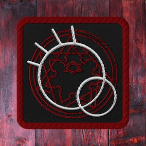 Puede incluir: Un parche bordado negro y rojo con un círculo blanco y una estrella en su interior. El círculo está rodeado por una serie de círculos concéntricos.